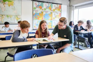 Leerlingen en docent van het Kamerlingh Onnes kijken samen in een lesboek.